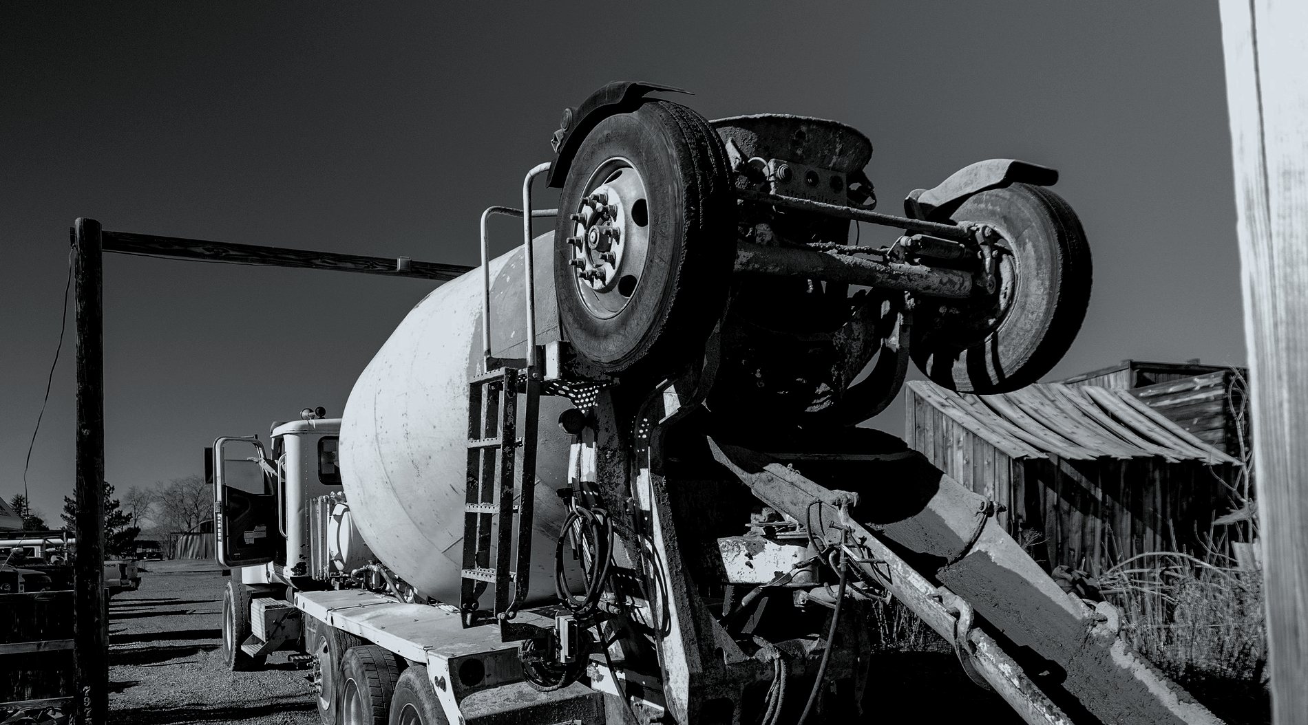A ready mix truck parked on gravel with its chute swung out and hand tools laid on the ground beside it.