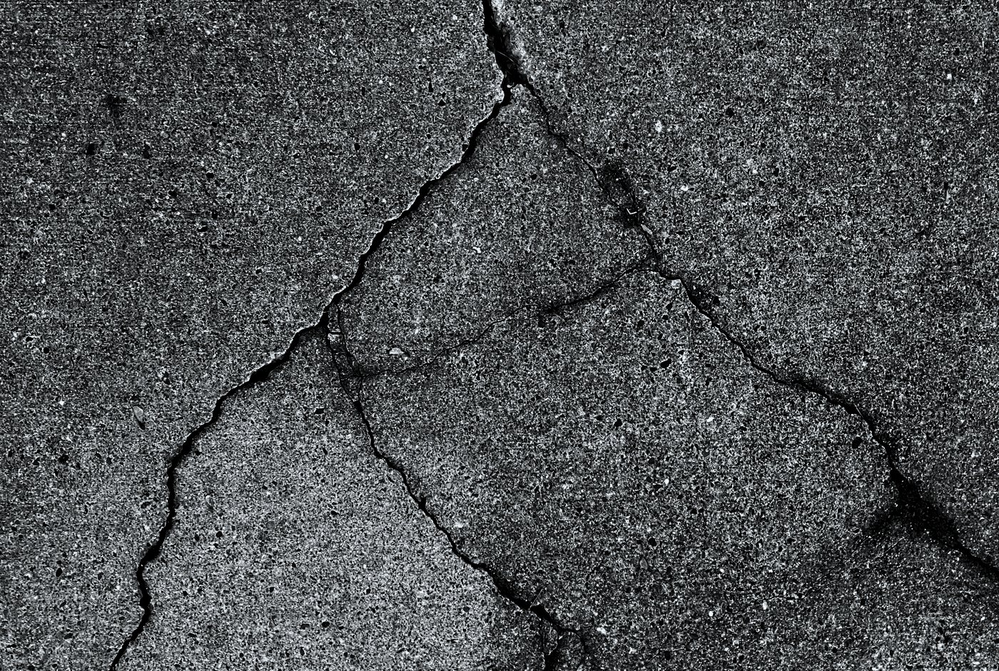 A branching network of fine cracks across a weathered driveway slab.