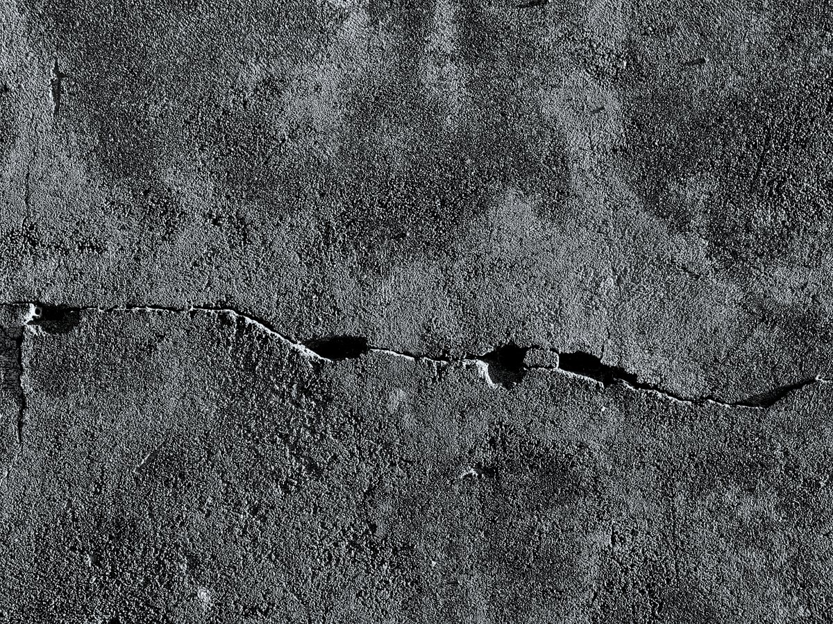 An open crack running the full width of an old concrete slab, with the edges spalled away on both sides.